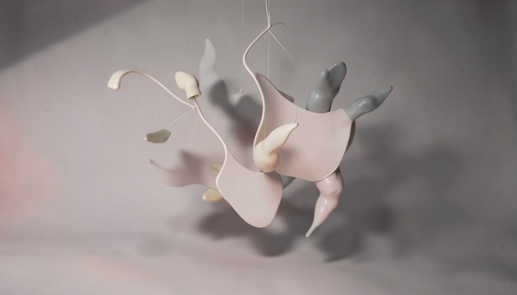 Composizione scultorea con elementi sospesi nei toni del bianco, grigio perla e beige, resa in duotono.