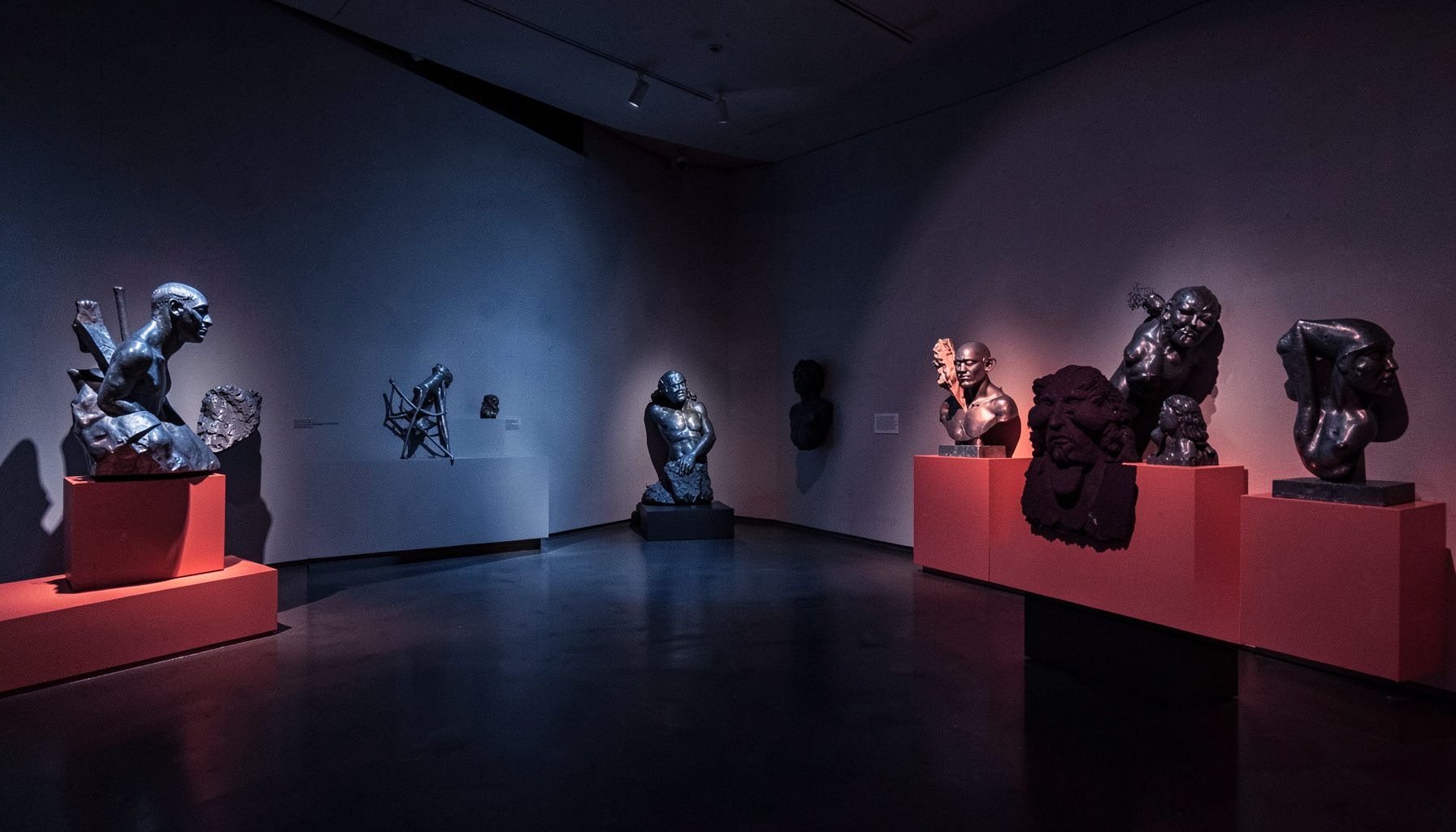 Scorcio di una mostra con sculture contemporanee illuminate, toni blu acciaio e tocchi di rosso.